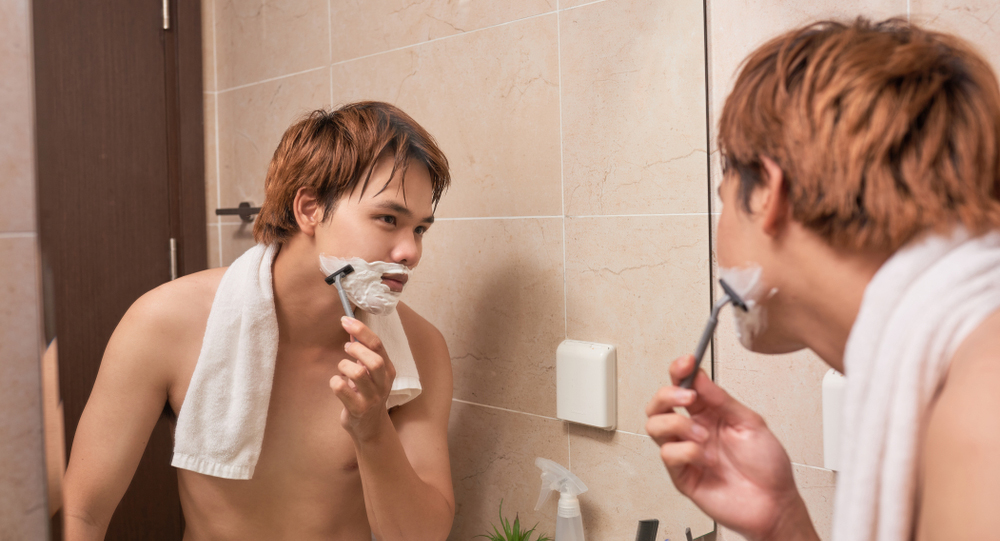 洗面台の鏡の前で髭剃りをする男性