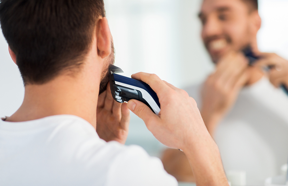 鏡を見ながらシェーバーで髭を剃る男性